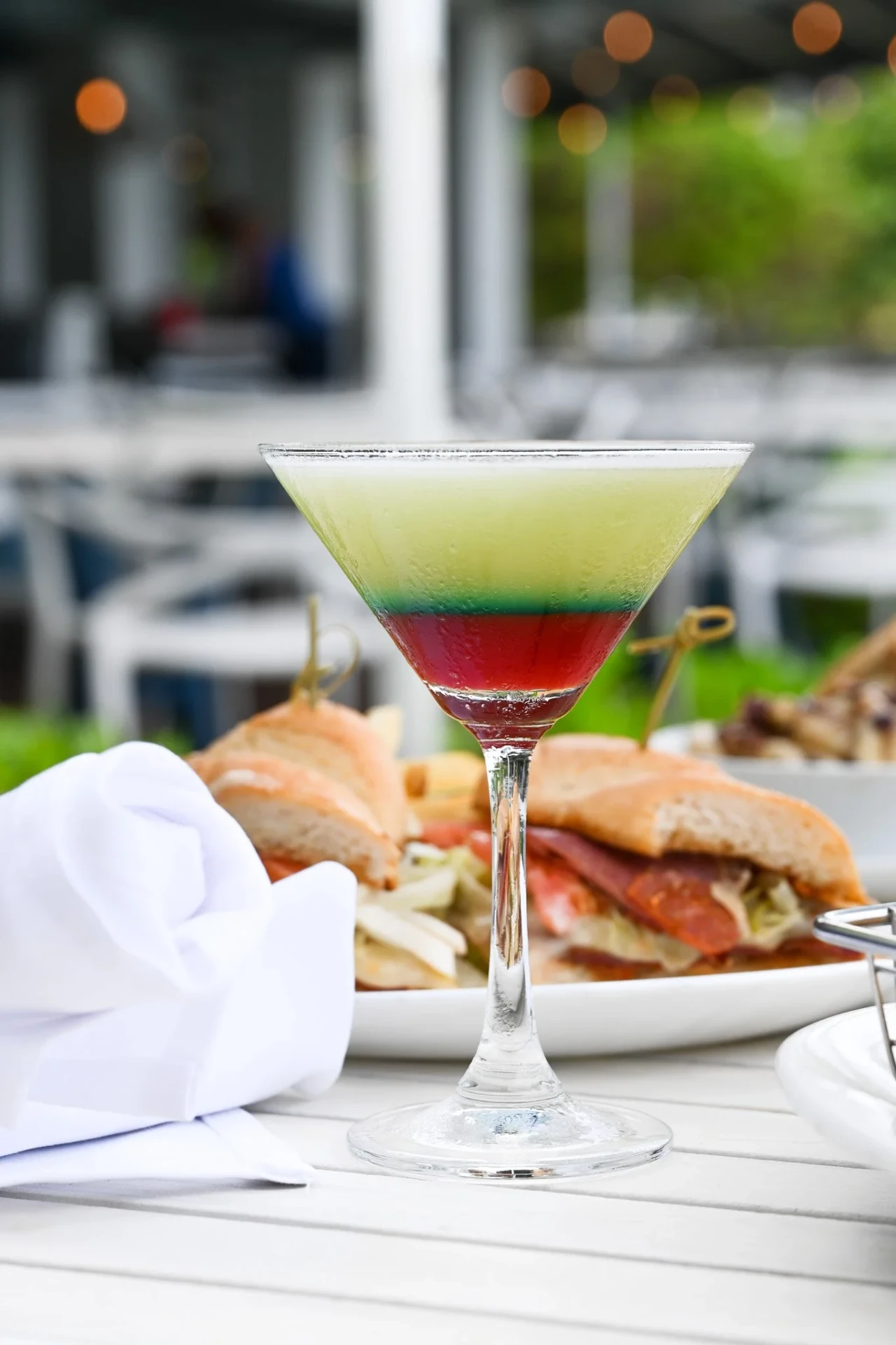 A colorful cocktail and Italian sandwich on a waterfront table