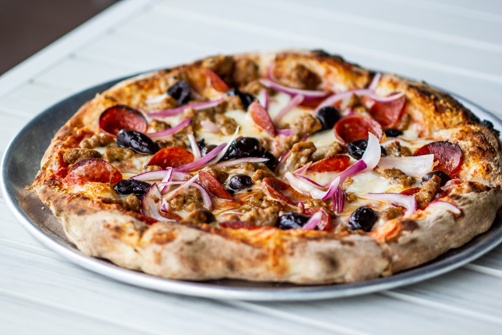 Naples-style pizza with pepperoni, sausage, olives and red onion