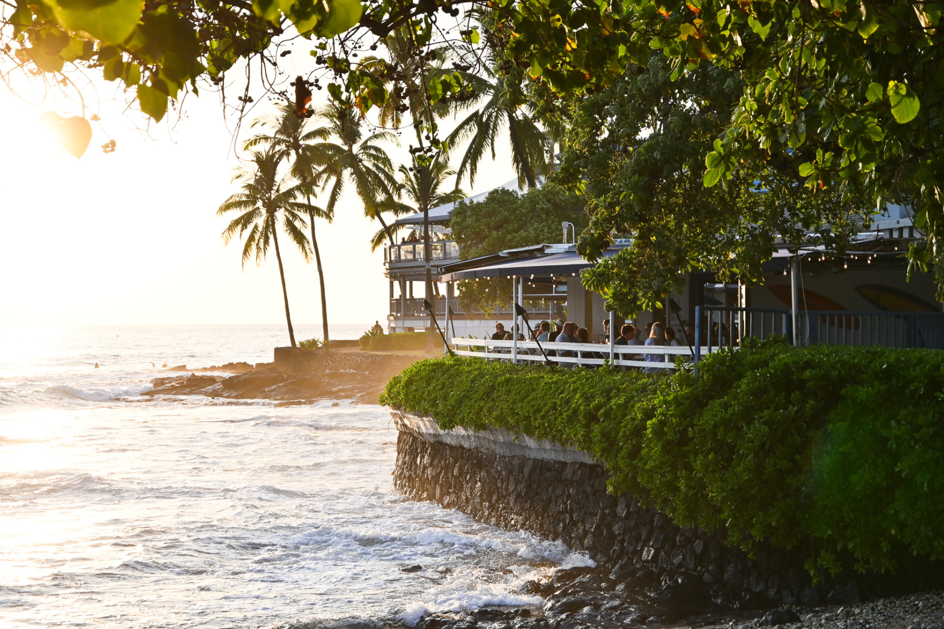 Kai's oceanfront deck above Oneo Bay with waves and palms at golden hour