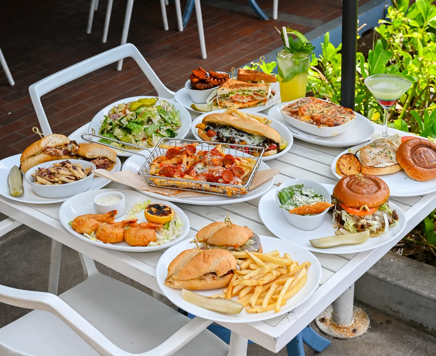 A waterfront table spread with Kai sandwiches, burgers, salads and cocktails