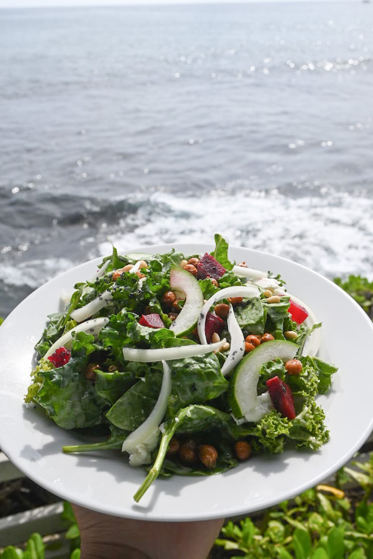 Kale and apple salad with crispy chickpeas held above the ocean