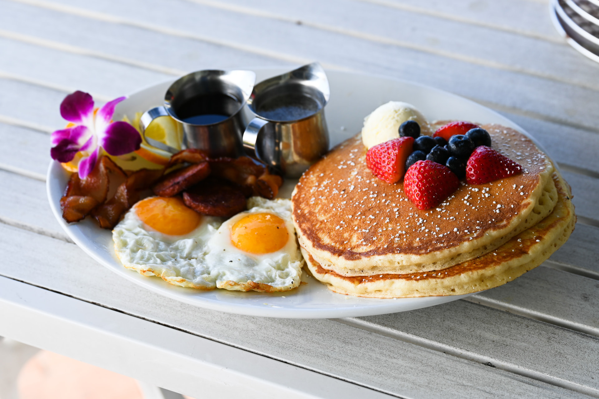 Brunch plate of pancakes with berries, eggs and bacon on the lanai