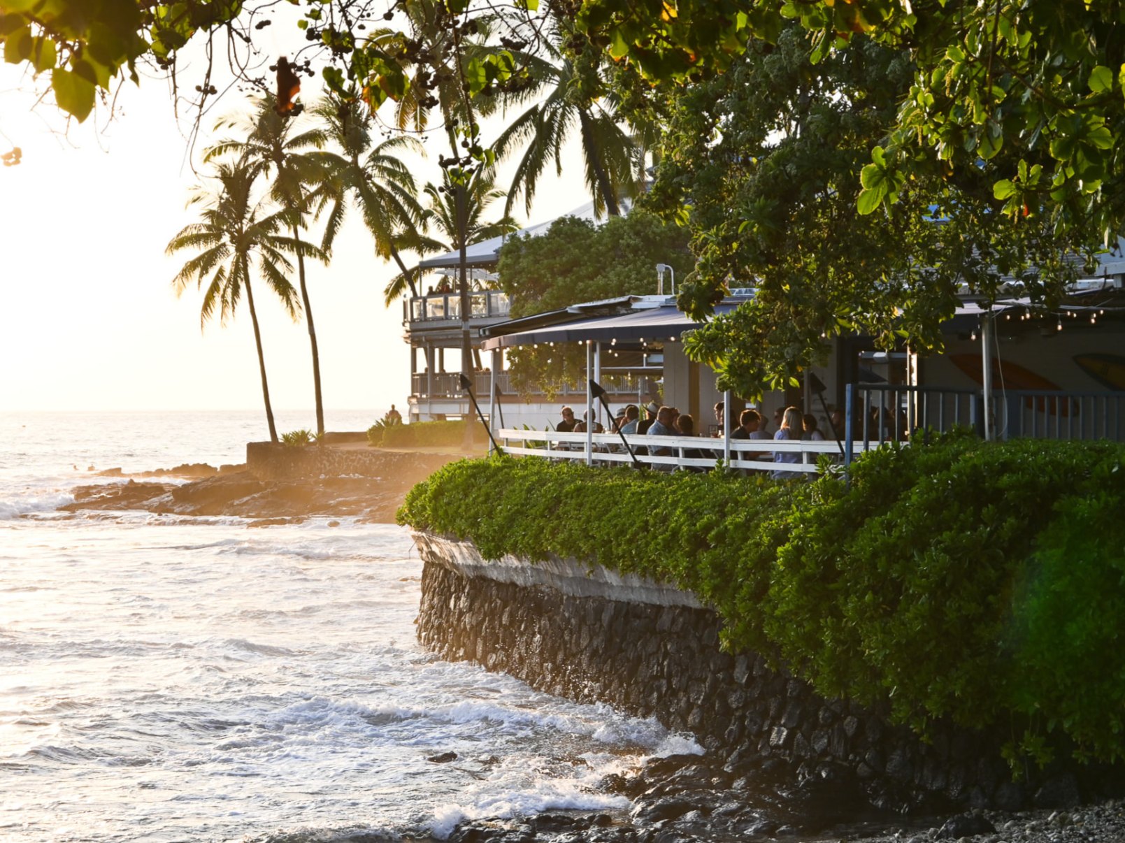 Kai's oceanfront deck above Oneo Bay with waves and palms at golden hour