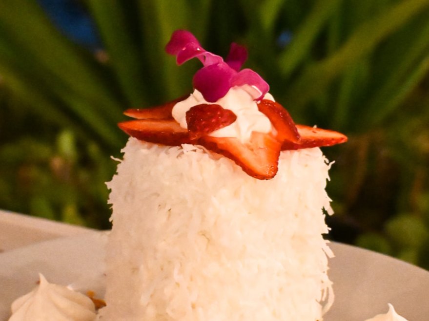 Tall coconut cake with strawberries and whipped cream in the evening