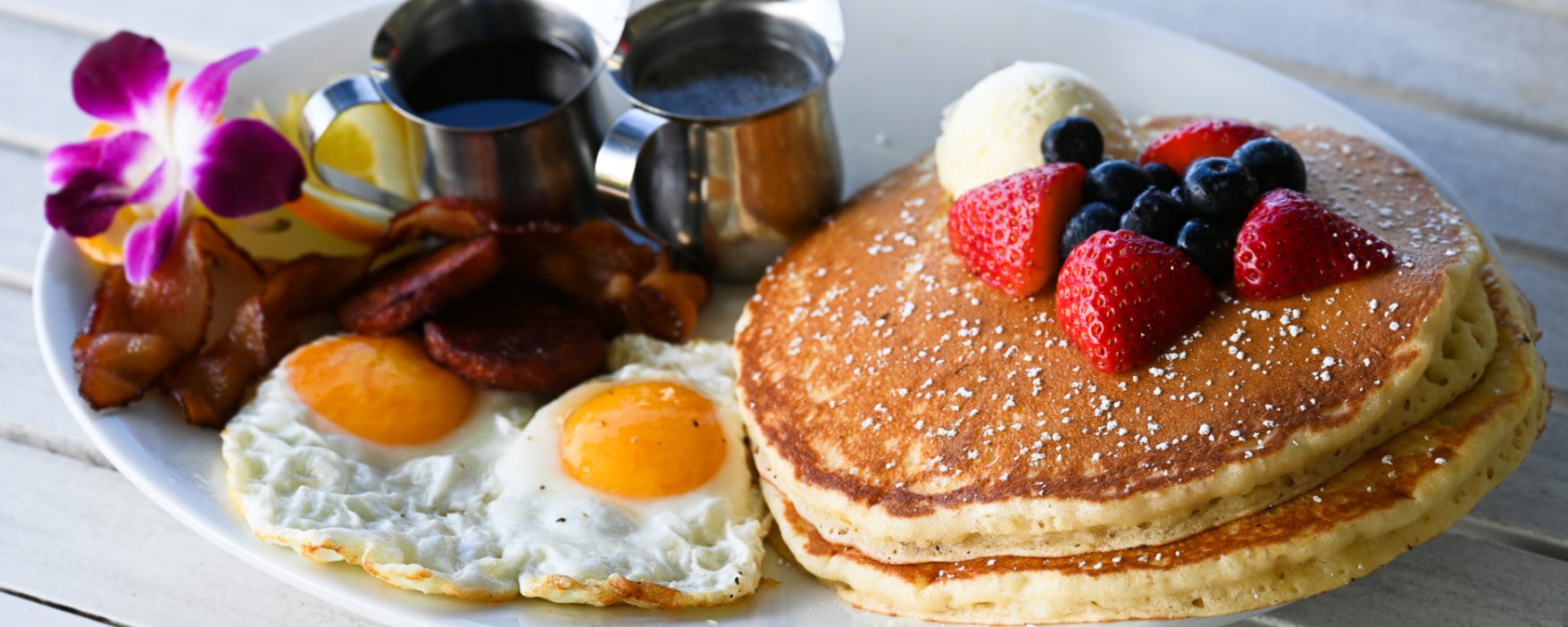 Brunch plate of pancakes with berries, eggs and bacon on the lanai