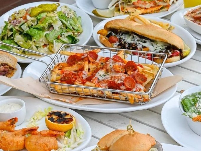 A waterfront table spread with Kai sandwiches, burgers, salads and cocktails